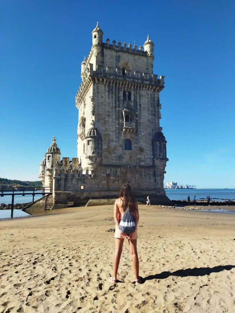 Niña de espaldas en una playa con una torre al fondo